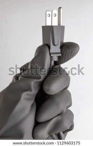 concept of energy dependence: a plug and cable in the person's hand, a black protective glove