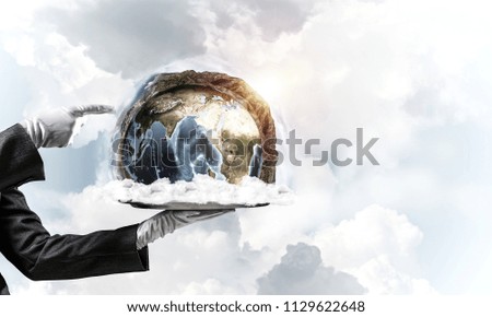 Cropped image of waitress's hand in white glove presenting Earth globe on metal tray and pointing on it with cloudy skyscape on background. 3D rendering. Elements of this image are furnished by NASA.