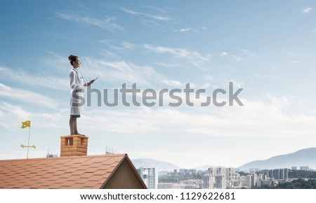 Confident medical industry employee in white suit standing at the top of building roof and holding tablet in hands. Skyscape and city view on background. Medical sphere concept