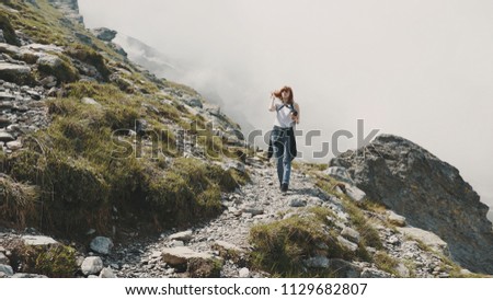 A young woman hiker walks in the mountains with photo camera. Transfagarasan, Carpathian mountains in Romania