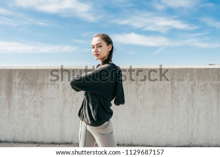 A sporty stylish girl in a black sweatsuit kneads muscles before training under the blue sky Royalty-Free Stock Photo #1129687157