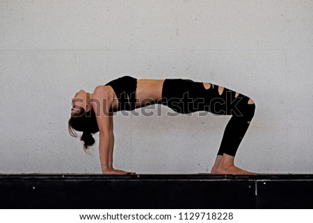Woman in dark sportswear practicing yoga with wall behind background