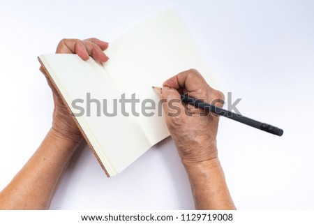 Senior woman's right hand with grey pencil writing on notebook isolated on white background, Stationery concept