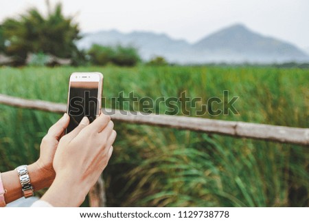 Close up woman holding a smartphone is take a beautiful photo view of the meadow and mountains. in thailand