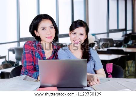 Two pretty college students smiling at the camera while studying together in the classroom