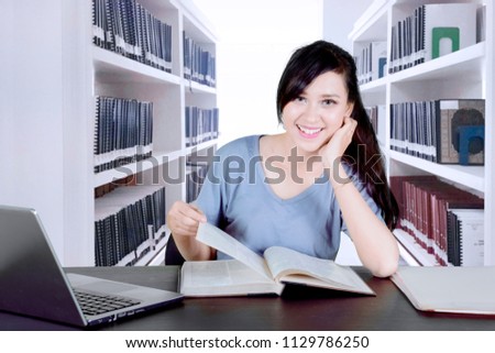 Picture of a beautiful college student smiling at the camera while studying in the library