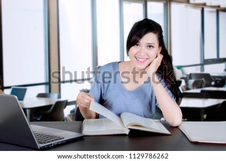 Picture of a beautiful college student smiling at the camera while reading a book