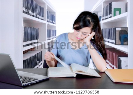 Picture of Caucasian female college student reading a book while sitting in the library