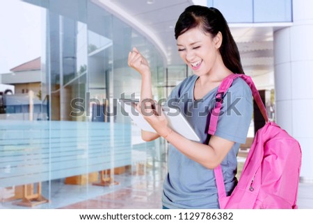 Picture of Caucasian female student celebrating her success while holding a digital tablet