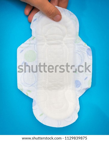 Woman is holding sanitary napkin in hand on blue background - menstrual hygiene concept