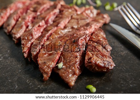 Thick Slices of Hot Grilled Whole Machete Steak or Skirt Steak on Black Stone Background. Fresh Juicy Medium Rare Beef Grillsteak. Barbecue Meat Top View Close Up Royalty-Free Stock Photo #1129906445