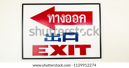 guidance label of exit in three languages, thai, english and chinese languages with red arrow to go left on the whit wall for instruction route for tourism.