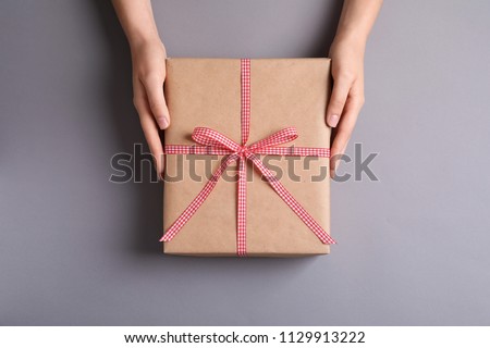 Woman holding gift box on grey background, top view