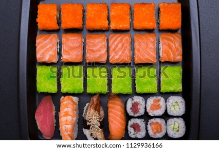 Japanese sushi rolls in the shape of a line on black plate background top view