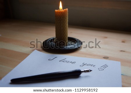 The inscription I love you in the form of a letter by hand with a pen on white paper and a candle burning on the table. Love letter.