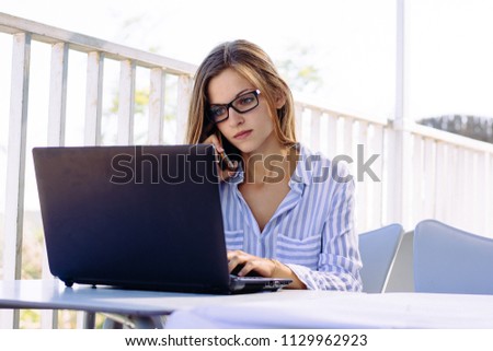 young woman working with laptop in terrace while calliing cell phone. Royalty-Free Stock Photo #1129962923