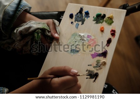 Artist with palette of oil paints. Painter with equipment and colors on workspace. Close up