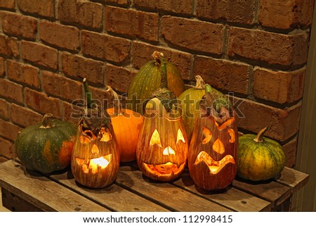 Carved eggplant jack o'lanterns with pumpkins and other squashes on a small table in front of a brick wall form part of a display for the halloween holiday