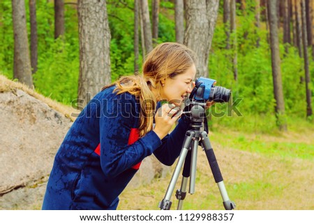 Girl taking a lifestyle picture for stock. Person shooting forest with a digital camera on tripod. Freelance photography job.