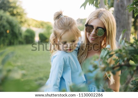 Young beautiful woman with her little cute daughter. Young daughter hugs mother in summer park