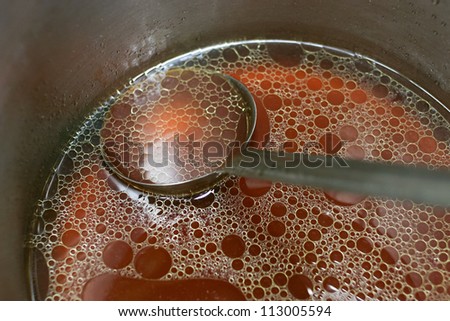 Close up shop of a pot of rich meat stock with a ladle