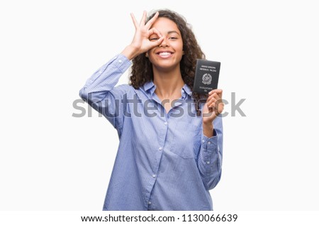 Young hispanic woman holding passport of Italy with happy face smiling doing ok sign with hand on eye looking through fingers