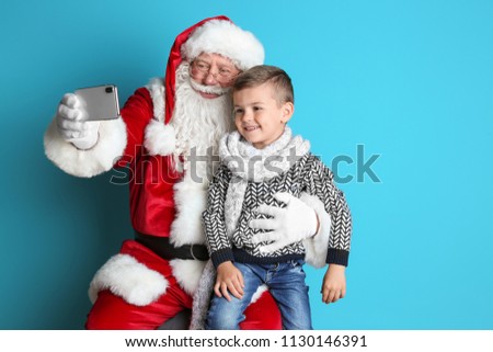 Authentic Santa Claus taking selfie with little boy on color background