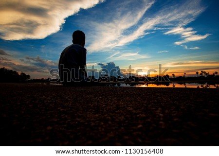 Silhouette Boy watching sky at sunset on the lake shore, beautiful sky