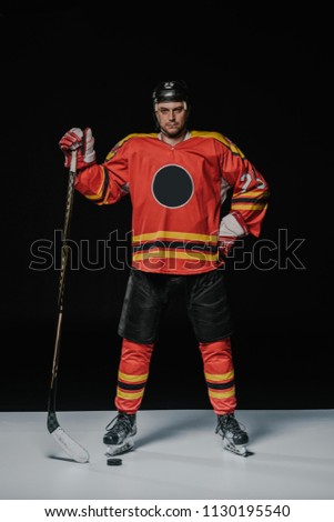 full length view of professional ice hockey player standing with hand on waist and looking at camera on black