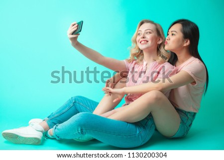 Portrait of a two joyful females taking a selfie while sitting isolated over blue background.