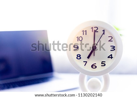 Clock white on white table with laptop ,in the morning sun light