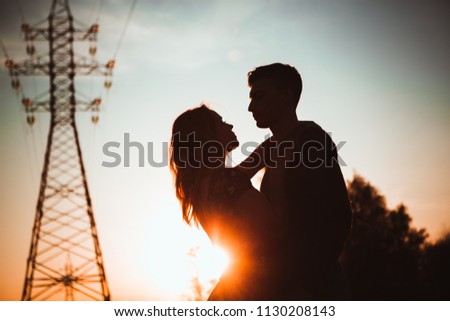 Silhouettes of a guy and girl in a field on a sunset background.