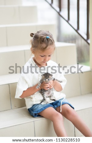 The little girl plays for four years with a kitten near the house