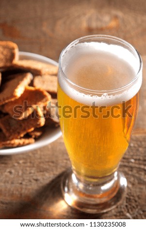 Light beer in a glass with snacks to beer in the background on a brown wooden background