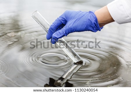 Researcher holds a test tube with water in a hand in blue glove Royalty-Free Stock Photo #1130240054