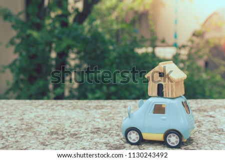 Close up wooden house and car toys on concrete floor with green trees and sunlight in the background. (Selective focus)