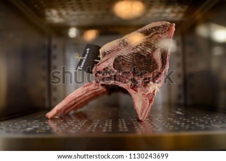 Dry aged barbecue Tomahawk steak on fridge in restaurant. Delicious gourmet raw meat in restaurant  Royalty-Free Stock Photo #1130243699
