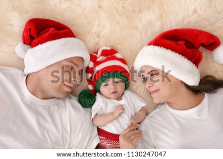 Happy couple with baby in Christmas hats on fuzzy rug, top view