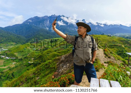 Happy young Asia man selfie with smart phone with beautiful Mount Kinabalu landscape scene at Kundasang, Sabah, Borneo