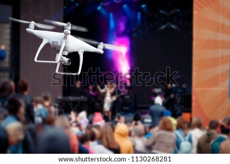 Drone of white color shoots recording concert, in background appears singer. Concept video technology. Royalty-Free Stock Photo #1130268281