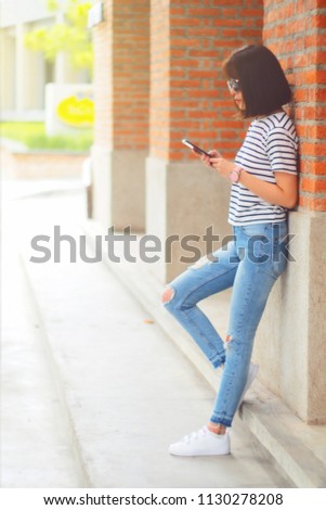 Portrait of cute asian teen woman using smartphone at outdoor. texting with someone. reading pleasant text message on mobile phone while happy smile chill out place. technology communication concept