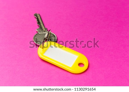 Yellow key tag on a purple textured cardboard background.The concept of rent, selling. Template. Trend colors