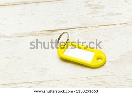Yellow key tag on a light tree textured background.The concept of renting, selling. Template. Trend colors
