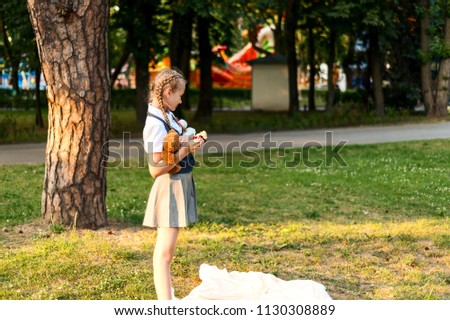 schoolgirl in uniform eating an apple in the park. student is holding soft bear toy