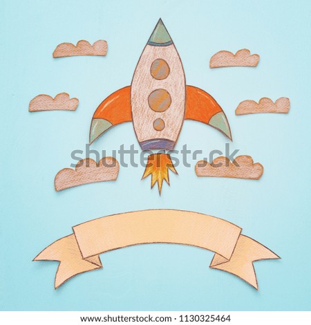 Rocket cut from paper and painted over wooden blue background
