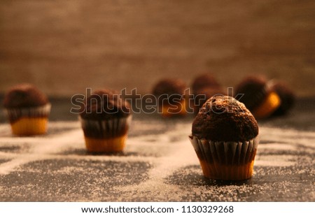 Straight On picture of three in a row game using small chocolate muffins, sugar as the lines, over dark surface, wood as background
