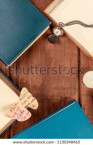 An overhead photo of old books, shot from above on a dark background with a vintage chain watch, a paper butterfly, and copy space