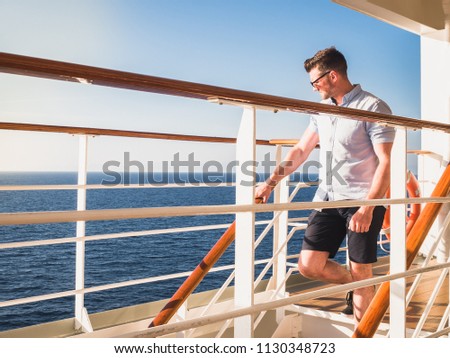 Attractive man in sunglasses on the top deck of a cruise ship looking out into the distance against the background of a sunset. Concept of sea travel and recreation