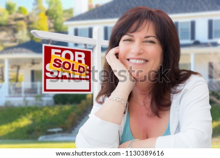 Middle Aged Woman In Front of House with Sold For Sale Real Estate Sign In Yard.