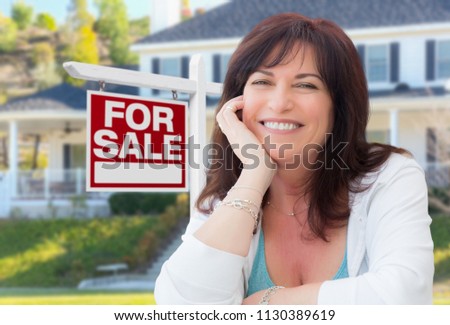 Middle Aged Woman In Front of House with For Sale Real Estate Sign In Yard.
